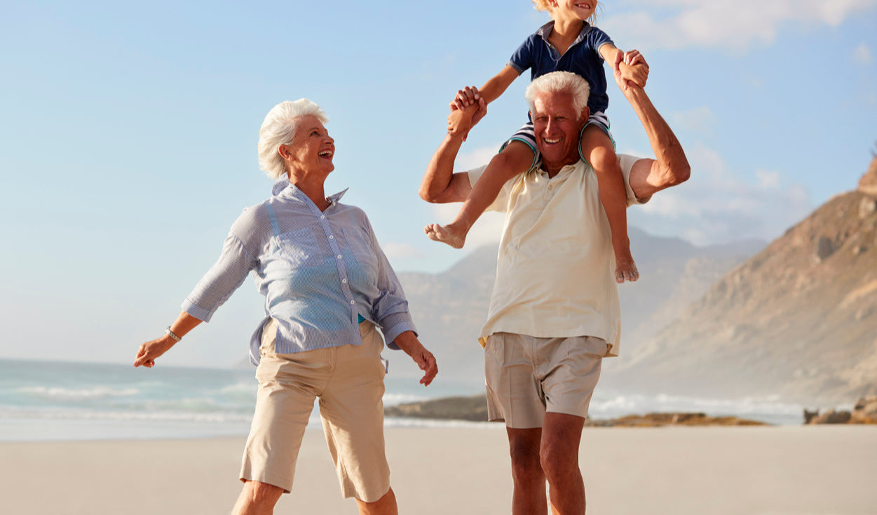 Senior couple walking on the beach, the grandfather free from hernia symptoms, with his grandchild on his shoulders.